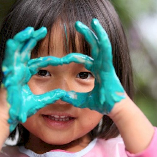 Ethnic minority girl making a heart to the camera with her blue paint covered hands