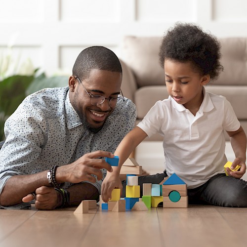BAME man playing with young BAME  boy on the flor with building blocks