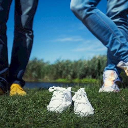 shot of two men's legs with a pair small shoes in between them on the grass