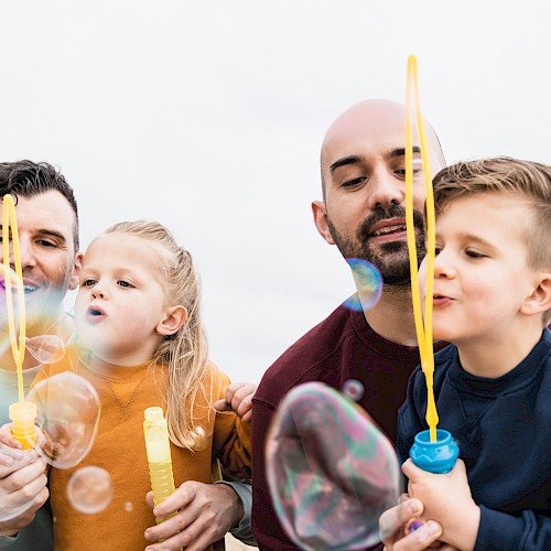 Smiling male couple with two children blowing bubbles
