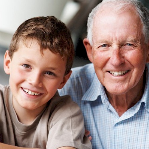 Older man sitting next to a pre-teen boy, smiling