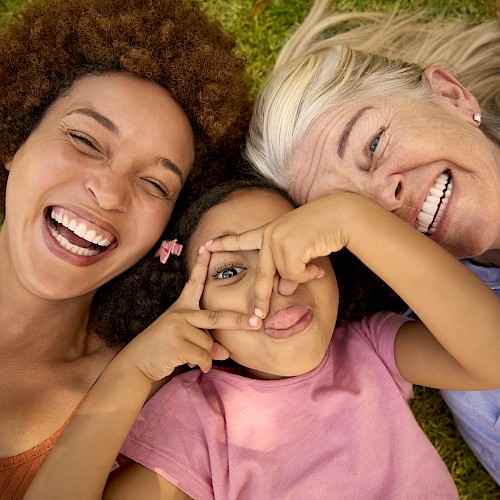 Two laughing women with a young girl sticking out her tongue between them on the floor