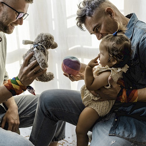 Gay male couple playing with a baby on their lap