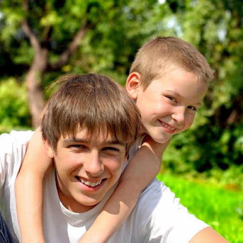 Older boy siblings outside on a sunny day embracing and smiling at the camera