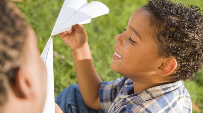 2 young boys playing with a paper airplane